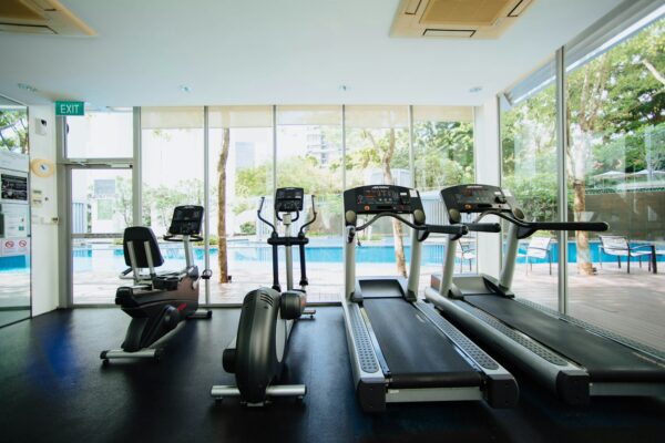 Treadmill dan sepeda statis berjajar di area gym dengan pencahayaan alami