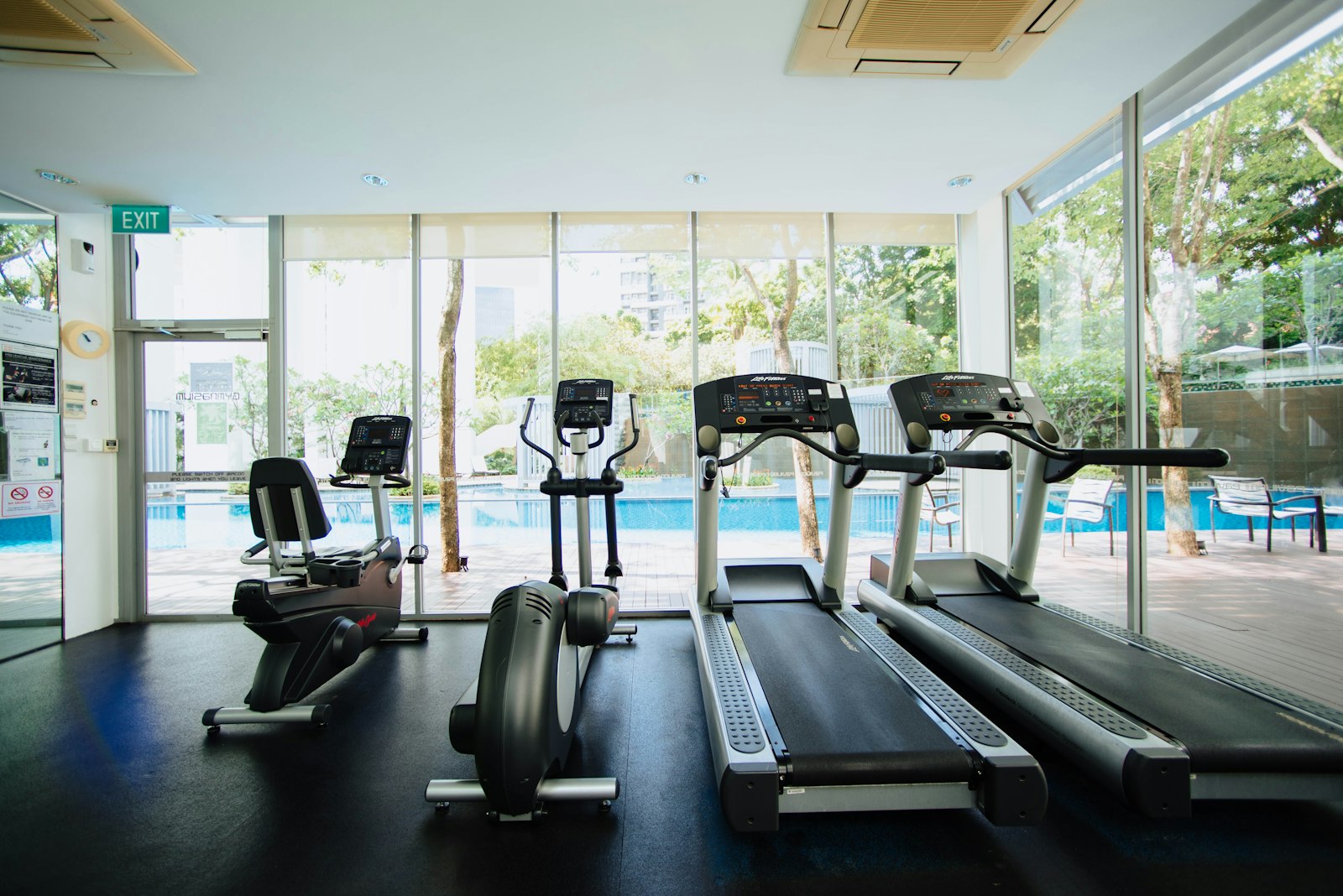 Treadmill dan sepeda statis berjajar di area gym dengan pencahayaan alami